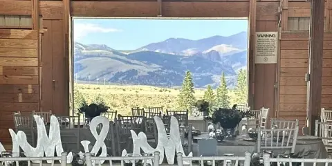 Interior of a wooden barn venue set up for a wedding reception with tables, chairs, and a mountain view through the open doorway.