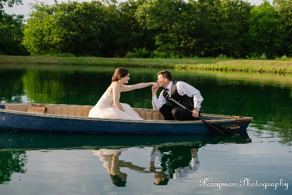 A bride and groom in a boat on a pond at a rustic wedding venue
