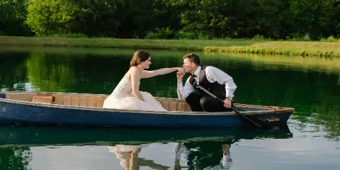 A bride and groom in a boat on a pond at a rustic wedding venue