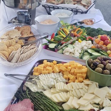A catering table set with a cheese and cracker platter, vegetable tray, and various dips.