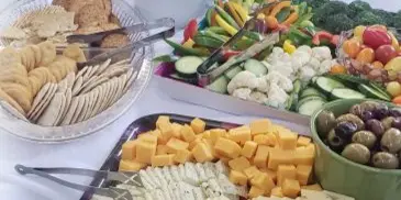 A catering table set with a cheese and cracker platter, vegetable tray, and various dips.