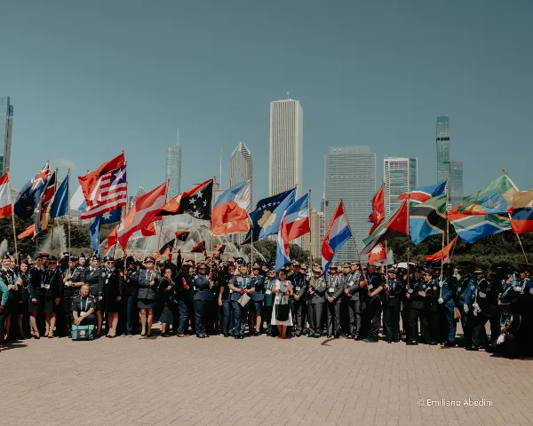 A large group of uniformed people holding international flags in a Chicago plaza with the city skyline in the background.