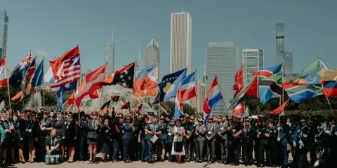 A large group of uniformed people holding international flags in a Chicago plaza with the city skyline in the background.