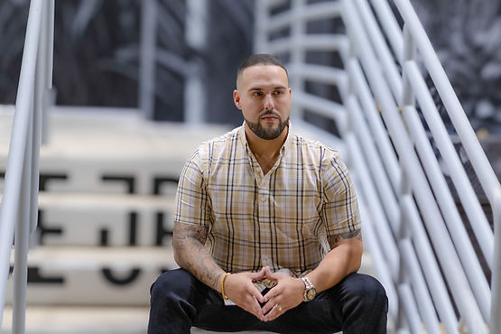 Portrait of Louie Forte, a photographer, sitting on stadium steps wearing a plaid shirt.