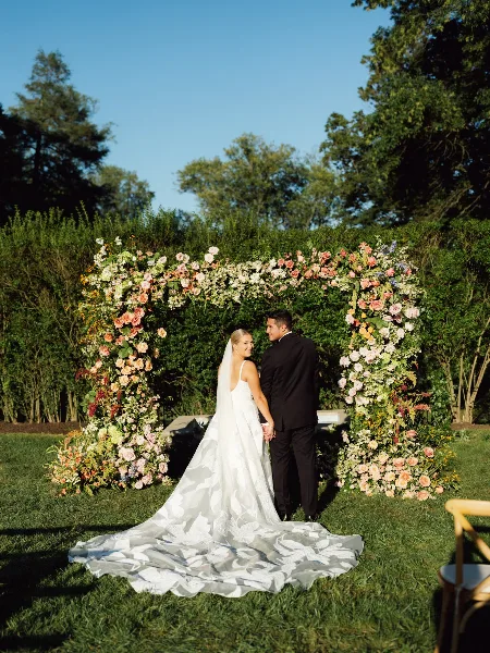 Bride and groom looking back during an outdoor garden wedding ceremony beneath a floral arch.