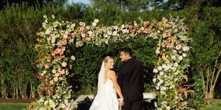 Bride and groom looking back during an outdoor garden wedding ceremony beneath a floral arch.