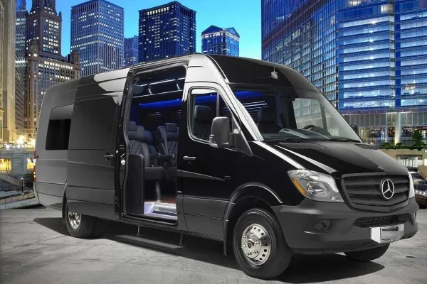 Black Mercedes Sprinter passenger van with side door open showing interior seats, parked in front of a city skyline.