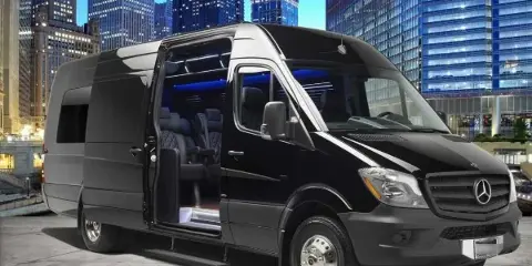 Black Mercedes Sprinter passenger van with side door open showing interior seats, parked in front of a city skyline.