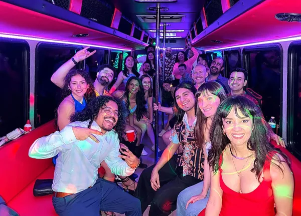 Interior of a party bus with colorful LED lighting and a group of smiling passengers.