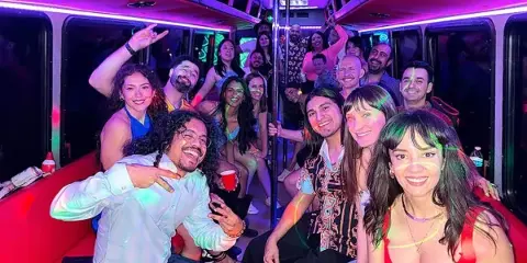 Interior of a party bus with colorful LED lighting and a group of smiling passengers.
