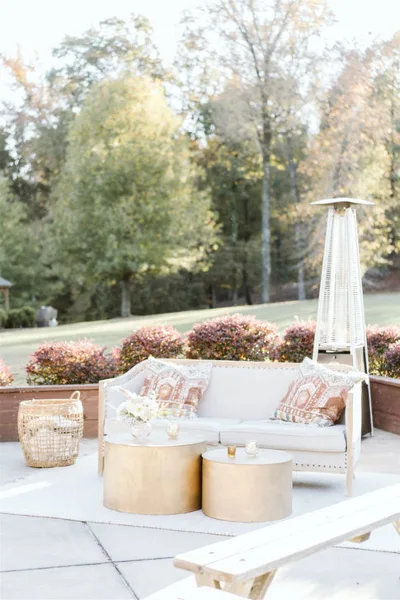 An outdoor event lounge setup featuring a white sofa, gold coffee tables, and a patio heater.
