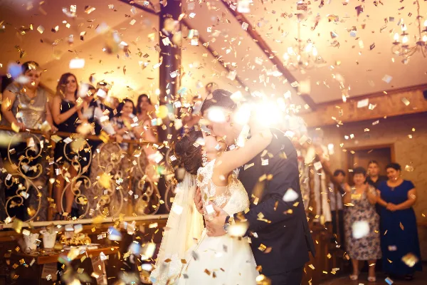A bride and groom dancing at a wedding reception while gold confetti falls around them.