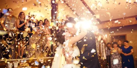 A bride and groom dancing at a wedding reception while gold confetti falls around them.