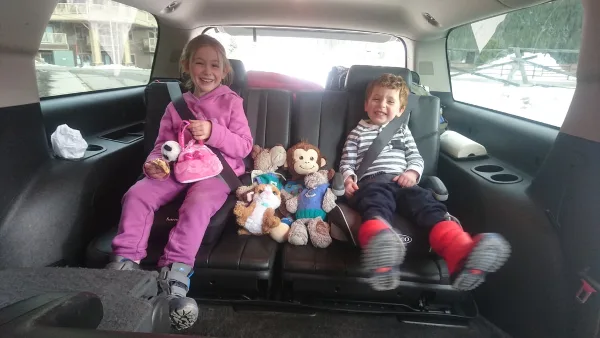 Two children sitting in the back seat of a passenger van with stuffed animals.