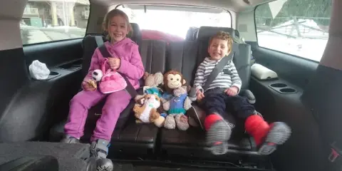 Two children sitting in the back seat of a passenger van with stuffed animals.