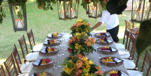 Outdoor wedding reception table set with plated food, floral centerpieces, and a catering staff member in a white shirt and black apron.