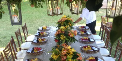 Outdoor wedding reception table set with plated food, floral centerpieces, and a catering staff member in a white shirt and black apron.