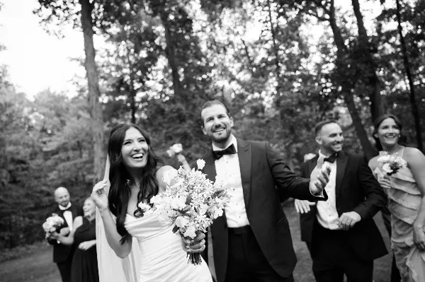 A black and white photograph of a bride and groom smiling and walking outdoors with their wedding party.