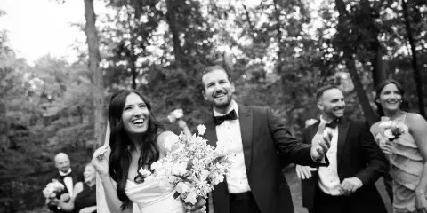 A black and white photograph of a bride and groom smiling and walking outdoors with their wedding party.