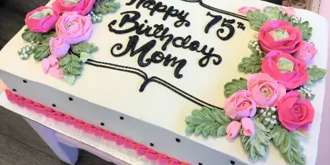 A white sheet cake decorated with pink and green piped roses and black lettering reading Happy 75th Birthday Mom.