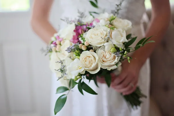 A bride in a white wedding dress holding a bouquet of white roses and pink accents.