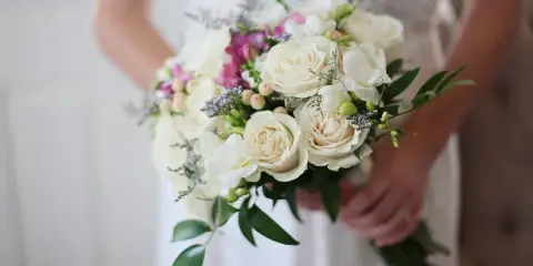 A bride in a white wedding dress holding a bouquet of white roses and pink accents.