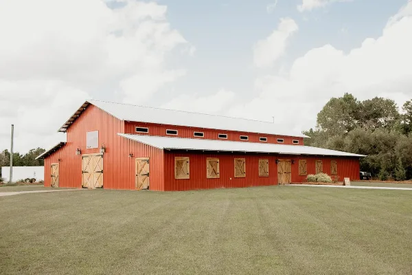 Exterior view of a large red barn with wooden doors and a metal roof on a grassy field.