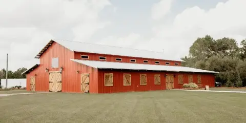 Exterior view of a large red barn with wooden doors and a metal roof on a grassy field.