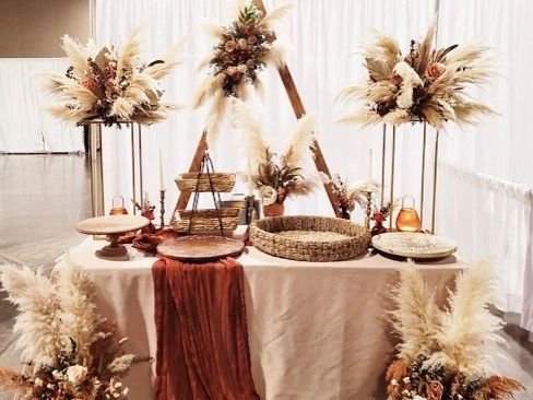 A professionally decorated event table featuring floral arrangements, pampas grass, and rustic centerpieces.