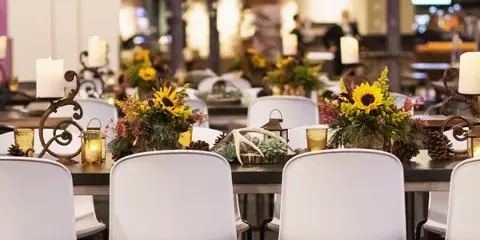 A close-up view of a decorated event table featuring white chairs, sunflower centerpieces, and candlelight.
