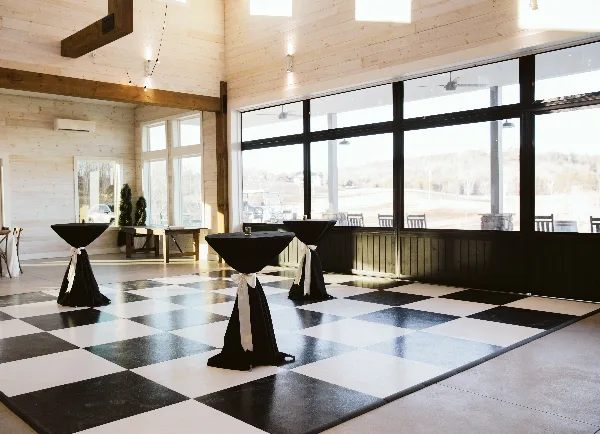 Interior view of a wedding venue reception hall with a black and white checkered dance floor and large windows.