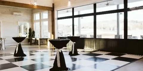 Interior view of a wedding venue reception hall with a black and white checkered dance floor and large windows.