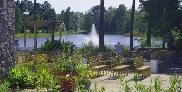 An outdoor wedding ceremony area with rows of chairs and a wooden arch overlooking a lake with a fountain.