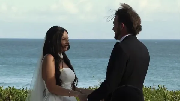A bride and groom facing each other during a wedding ceremony by the ocean.