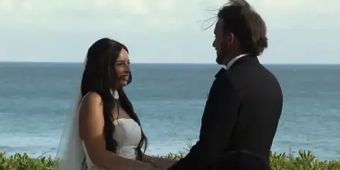 A bride and groom facing each other during a wedding ceremony by the ocean.