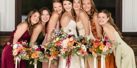 A bride and her bridesmaids posing together with bouquets, showcasing styled hair and makeup.