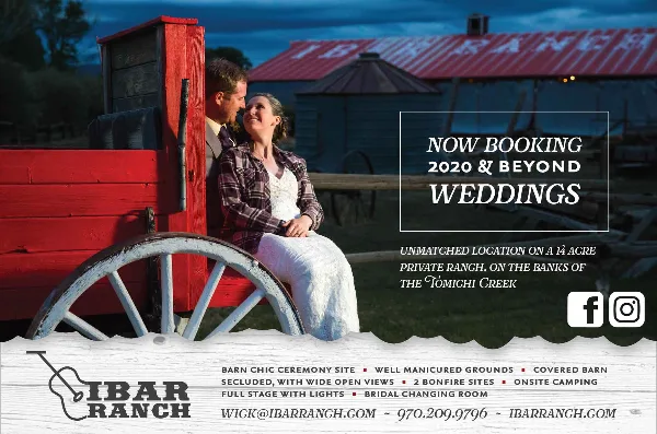 A couple sitting on a red wooden wagon in front of the I Bar Ranch barn at dusk.