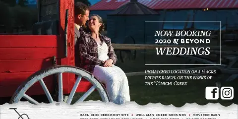 A couple sitting on a red wooden wagon in front of the I Bar Ranch barn at dusk.