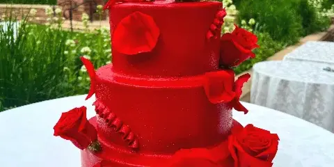 Three-tier red wedding cake decorated with red roses, photographed outdoors with mountains behind it.