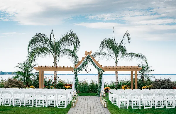 Outdoor wedding ceremony setup with white chairs and a floral arch overlooking a body of water.