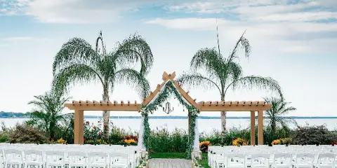 Outdoor wedding ceremony setup with white chairs and a floral arch overlooking a body of water.