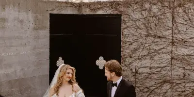 A bride in a white gown and a groom in a black tuxedo holding hands on a concrete staircase.