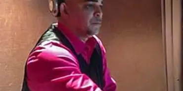 A professional DJ wearing headphones and a pink shirt, seated at a mixing console.