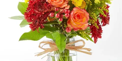 A colorful floral arrangement featuring orange roses, red chrysanthemums, and yellow filler flowers in a clear glass vase.