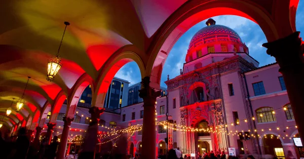 View of the Pima County Historic Courthouse dome and courtyard arches illuminated with red lighting at dusk.