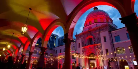 View of the Pima County Historic Courthouse dome and courtyard arches illuminated with red lighting at dusk.