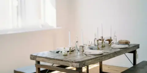 A rustic wooden table set with white candles, glassware, and folded napkins in a bright indoor venue space.