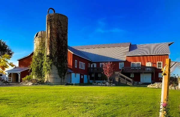Exterior view of a red barn wedding venue with a silo and green lawn under a blue sky