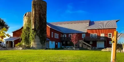 Exterior view of a red barn wedding venue with a silo and green lawn under a blue sky