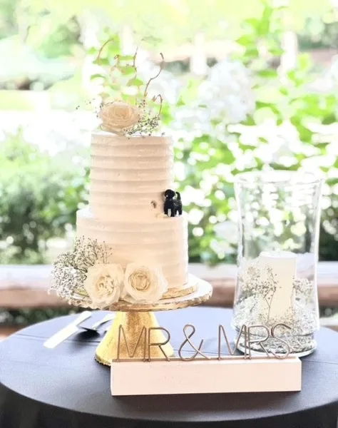 A two-tier white wedding cake with floral decorations and a Mr & Mrs sign on a table.